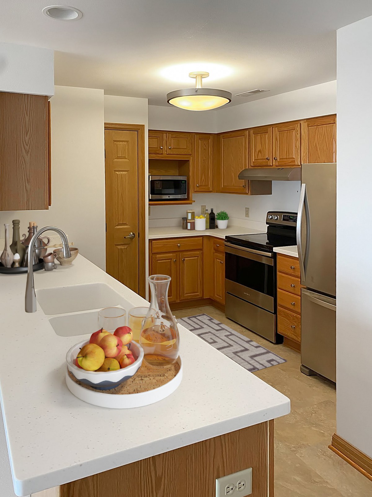 A modern kitchen with wooden cabinets, stainless steel appliances, and a clean white countertop featuring a fruit bowl.