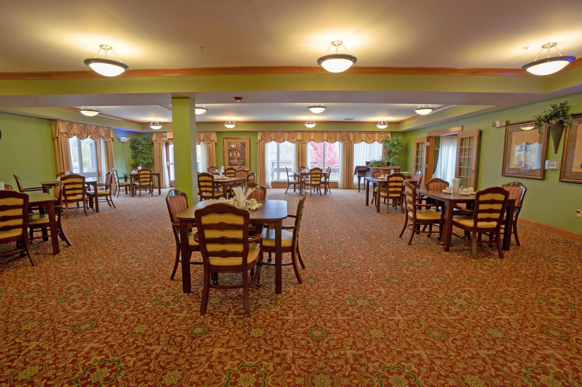 A spacious dining room with multiple tables and chairs arranged neatly under warm lighting.