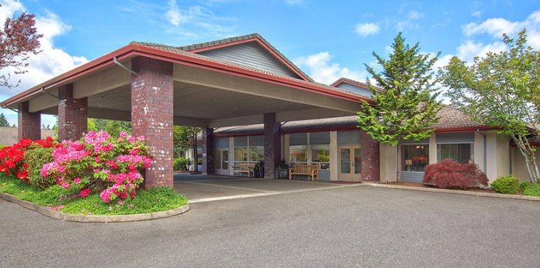 A building with a covered entrance and driveway surrounded by greenery.