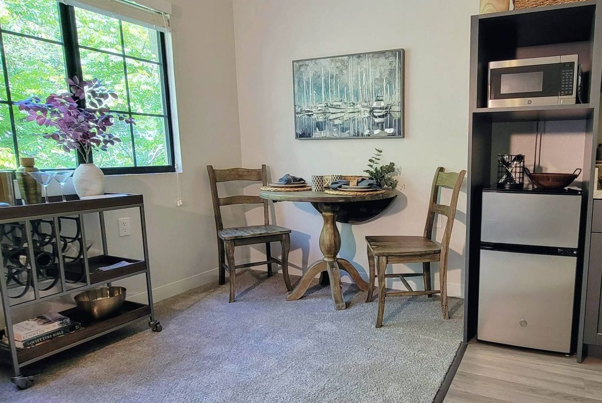 A cozy dining area with a small round table and two wooden chairs near a window.
