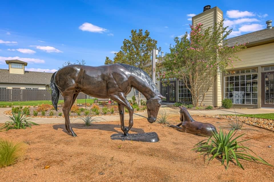 A bronze sculpture of a horse and a dog in an outdoor garden setting.