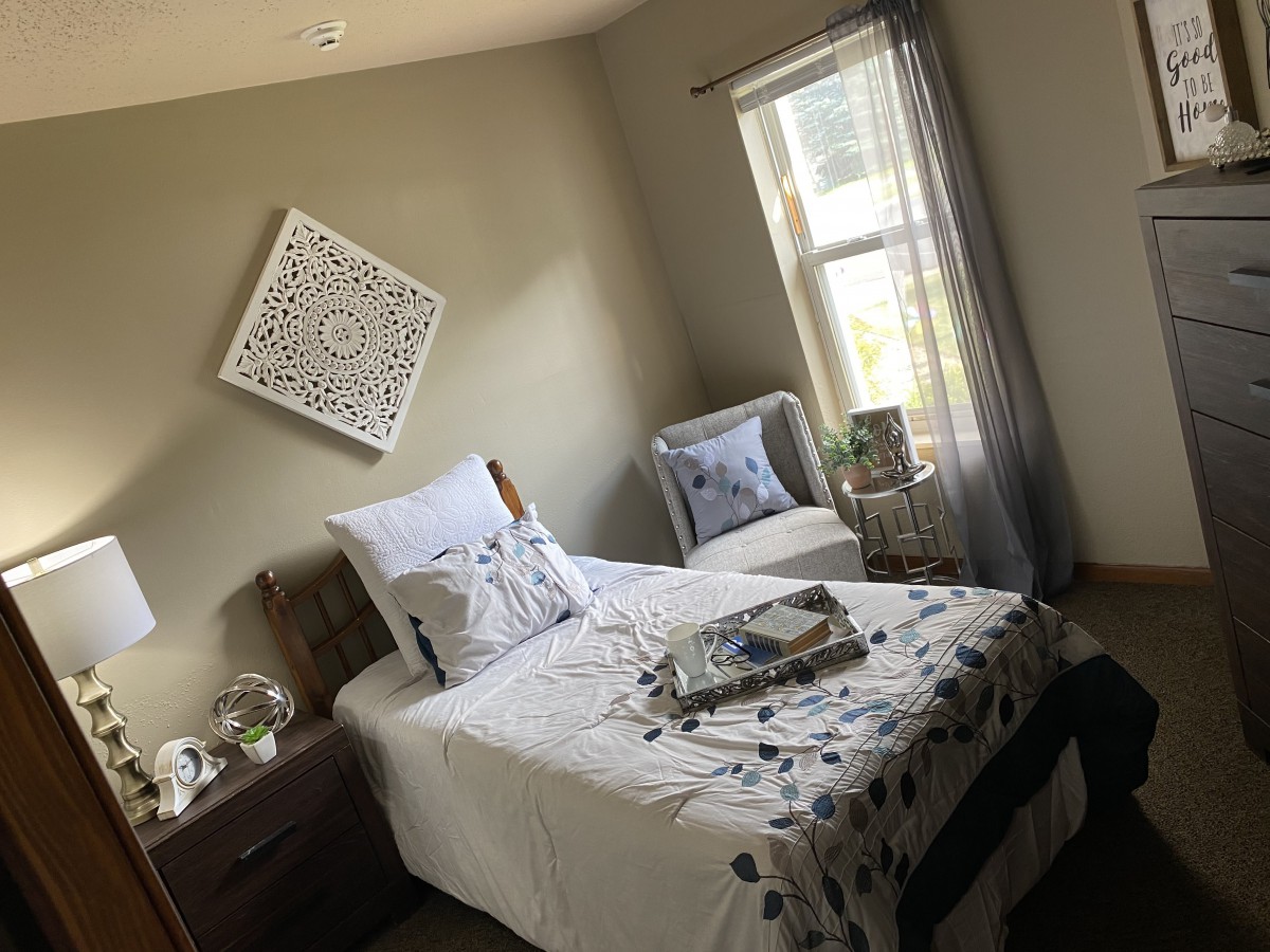 A cozy and modern bedroom with a single bed, decorative pillows, and natural light from the window.