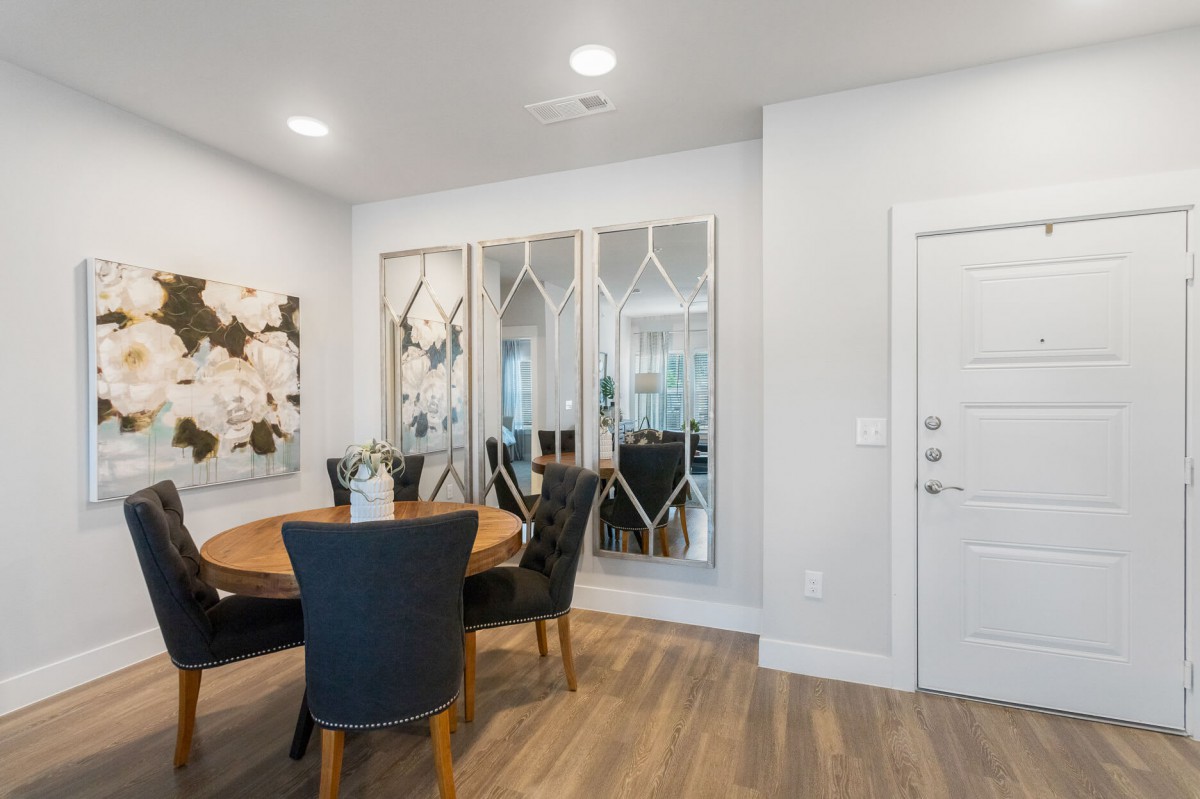 A modern dining room with a round table and elegant mirrors, featuring stylish artwork and wood flooring.
