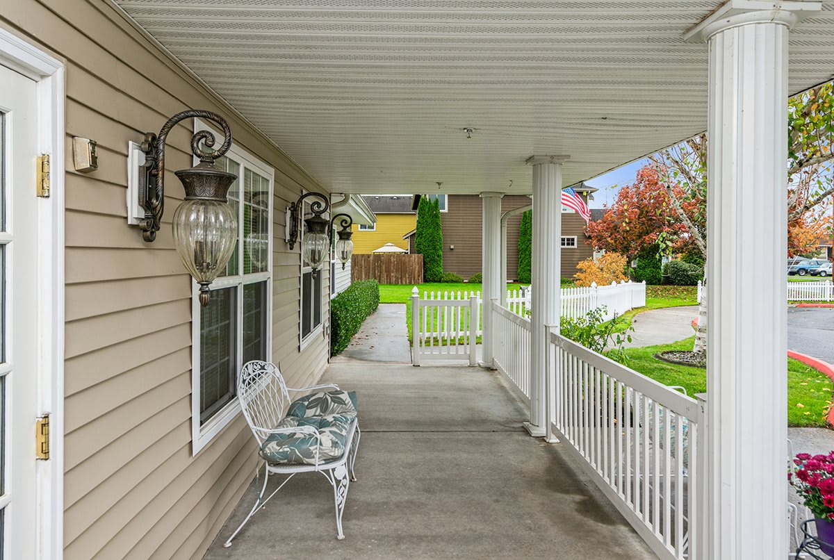 A cozy porch with a bench overlooking a yard and garden.
