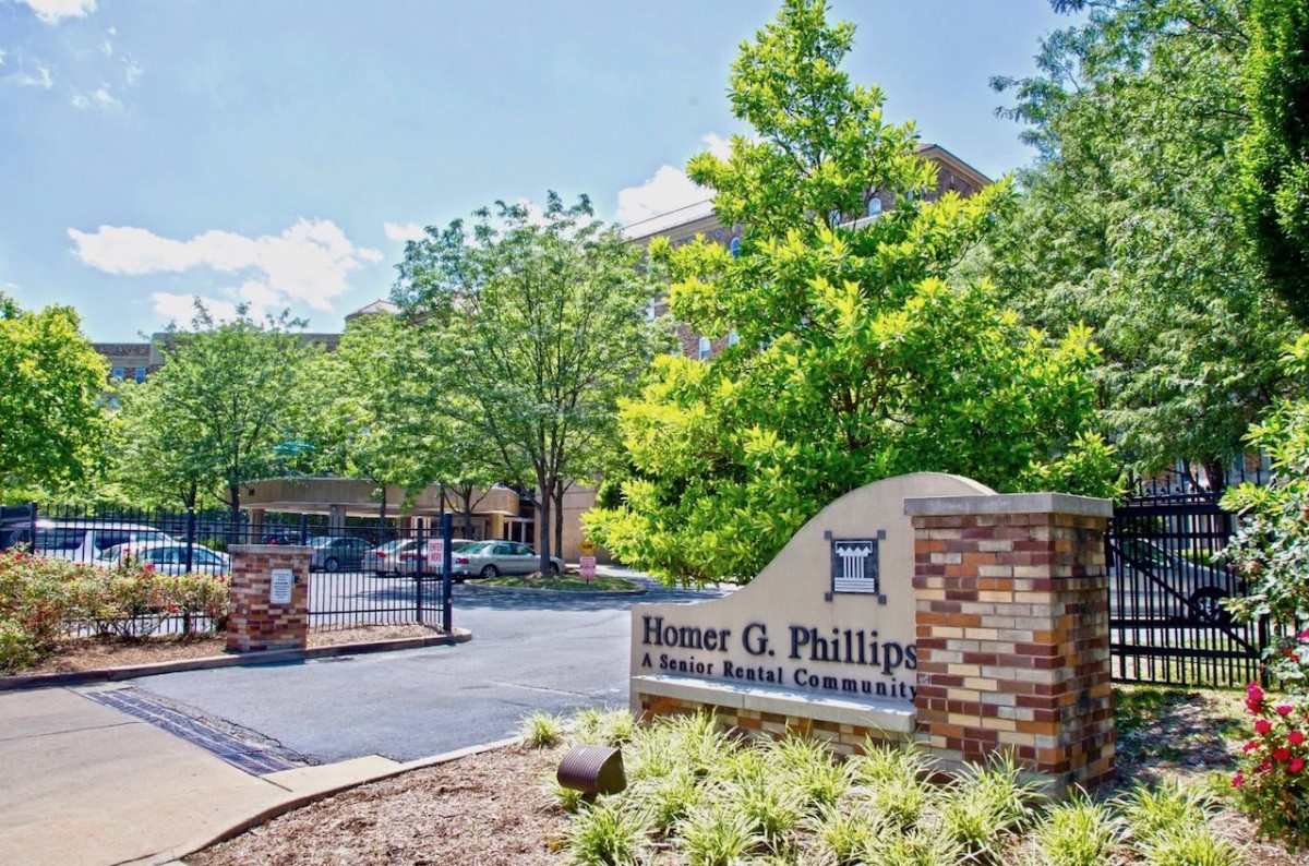 Entrance to a residential community with visible signage and surrounding greenery on a sunny day.