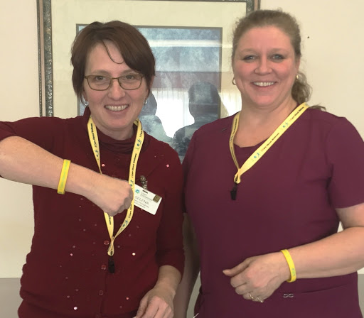 Two women proudly showing off their yellow accessories and smiling for the camera.