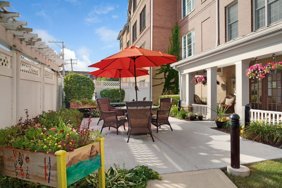 A cozy outdoor patio with a red umbrella, surrounded by lush greenery and comfortable seating.