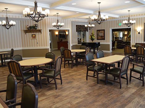 A spacious dining room with elegant chandeliers, wooden floors, and a grand piano.
