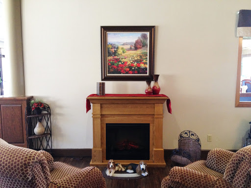 A cozy living room featuring a decorative fireplace, comfortable seating, and a beautiful landscape painting.