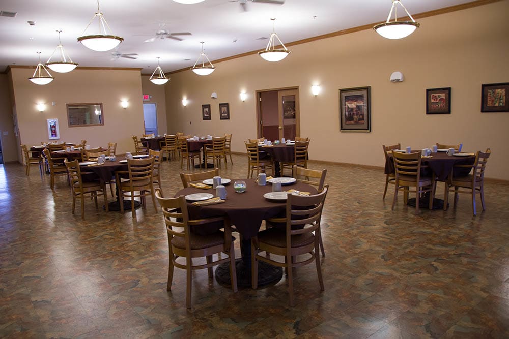 An empty dining room with several round tables and chairs arranged neatly.