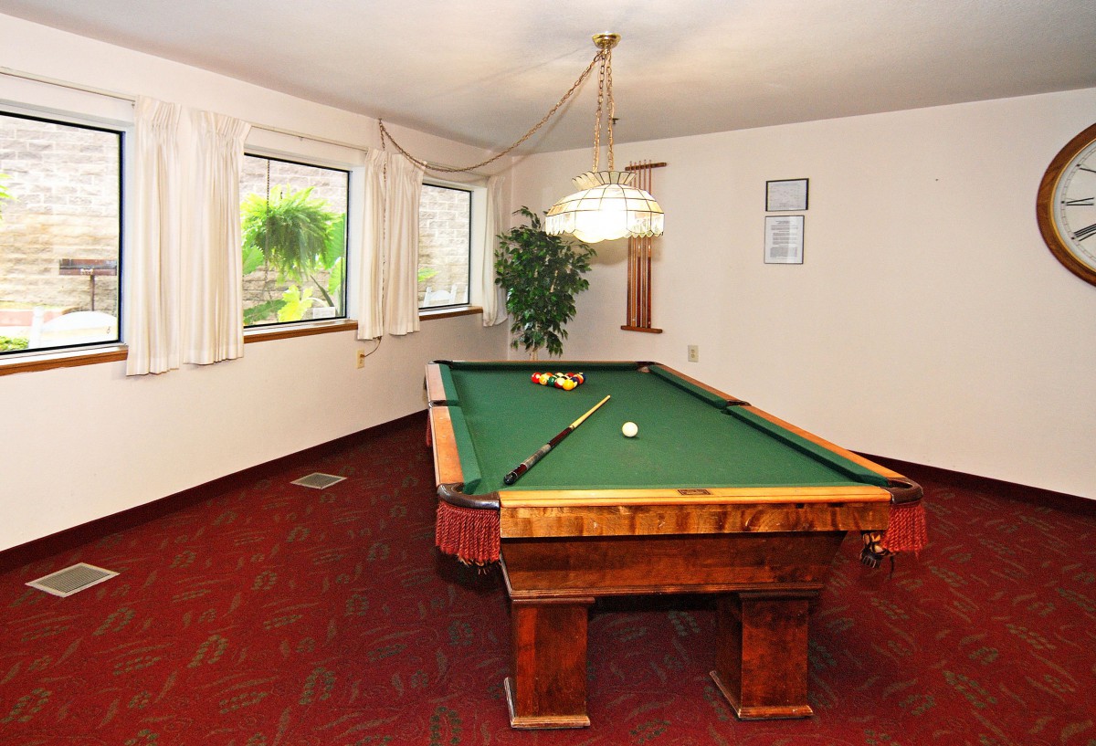 A cozy billiard room featuring a pool table with green felt and well-lit windows.