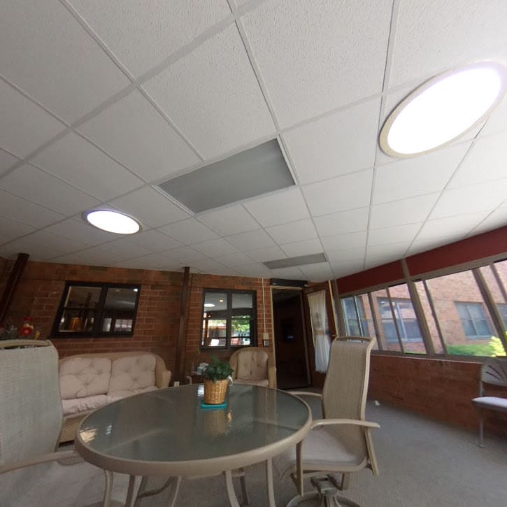 A modern office meeting room with a round table, chairs, and natural light from large windows.
