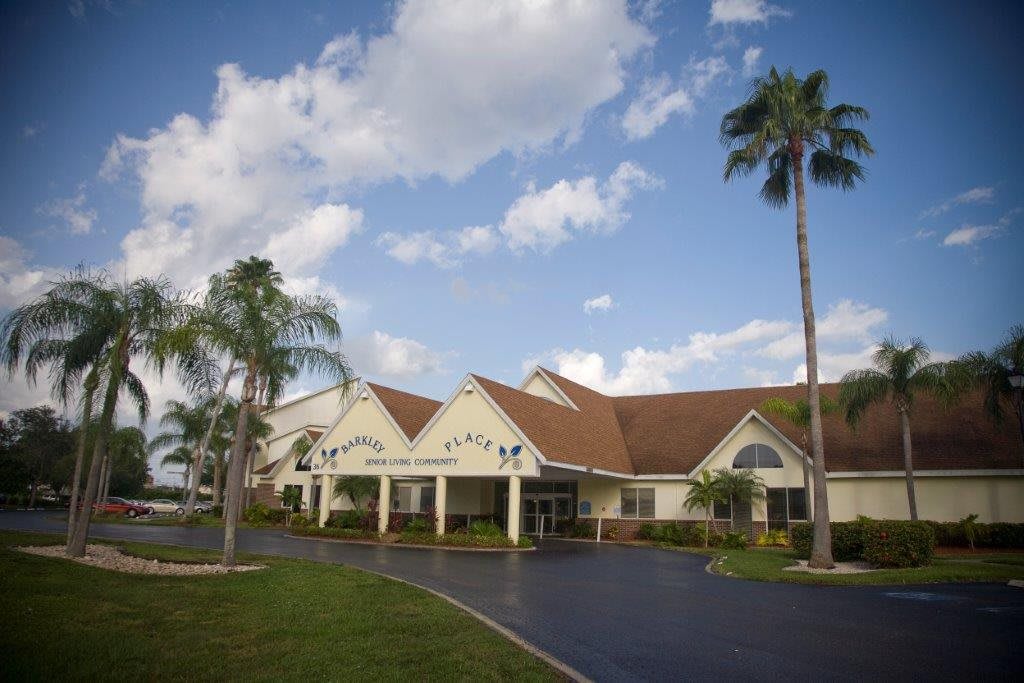 A healthcare facility featuring a landscaped driveway and surrounded by palm trees under a partly cloudy sky.