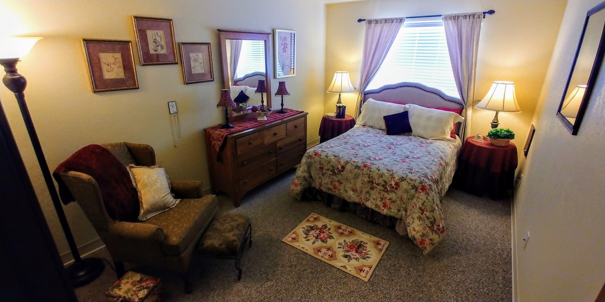 A cozy bedroom with traditional decor, featuring a floral bedspread, wooden dresser, and soft lighting.