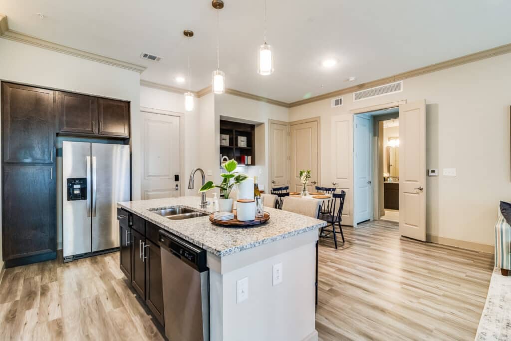 A modern kitchen with an island, featuring stainless steel appliances and wood flooring, adjacent to a cozy dining area.