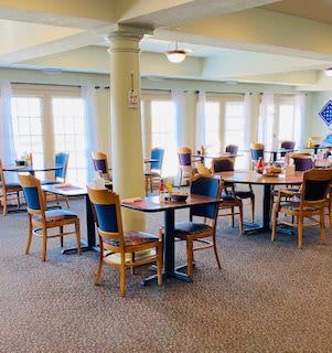 An empty dining area with neatly arranged tables and chairs, featuring large windows that brighten the space.