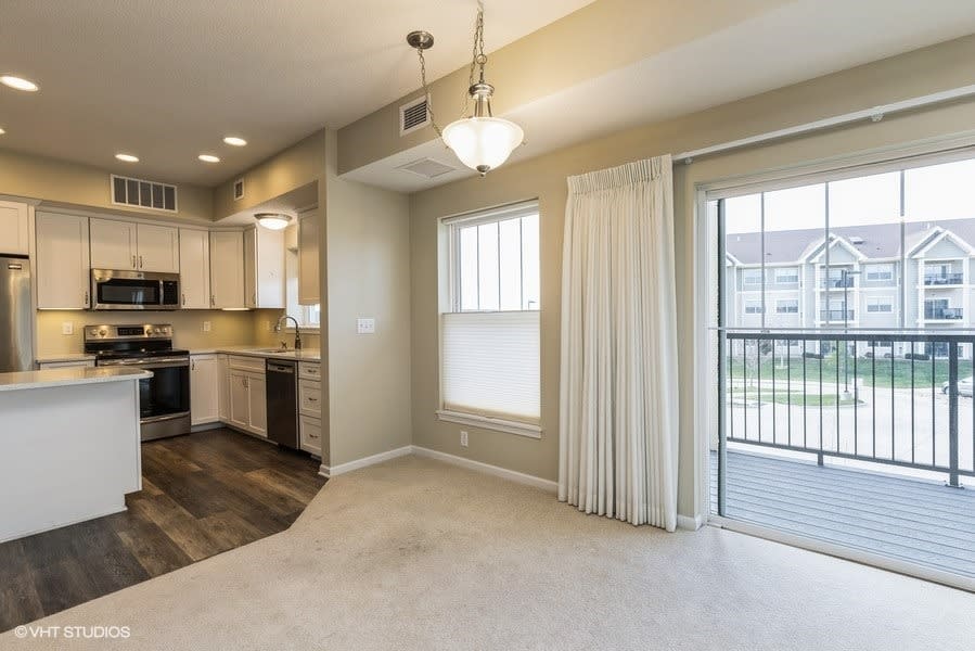 A modern apartment interior featuring a kitchen and dining area with natural light streaming through large windows.