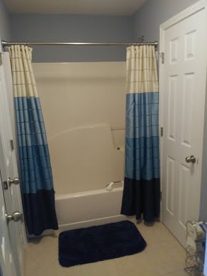 A bathroom with a bathtub featuring blue gradient shower curtains and a matching rug.