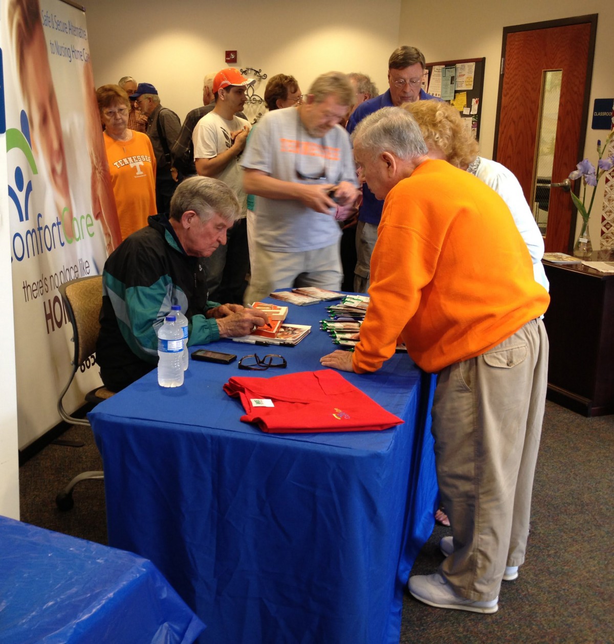 A book signing event with attendees gathered around a table for autographs.