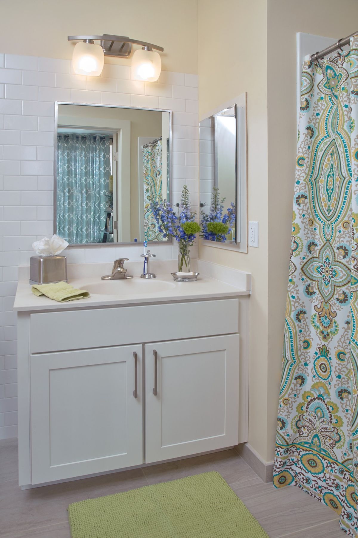 A modern bathroom with a white vanity, decorative shower curtain, and floral arrangement.
