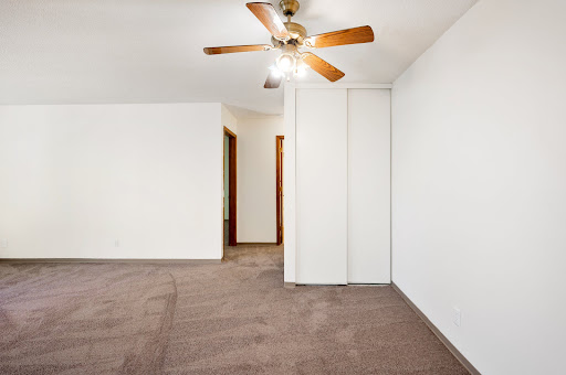 A spacious, empty bedroom featuring a ceiling fan and carpeted flooring.