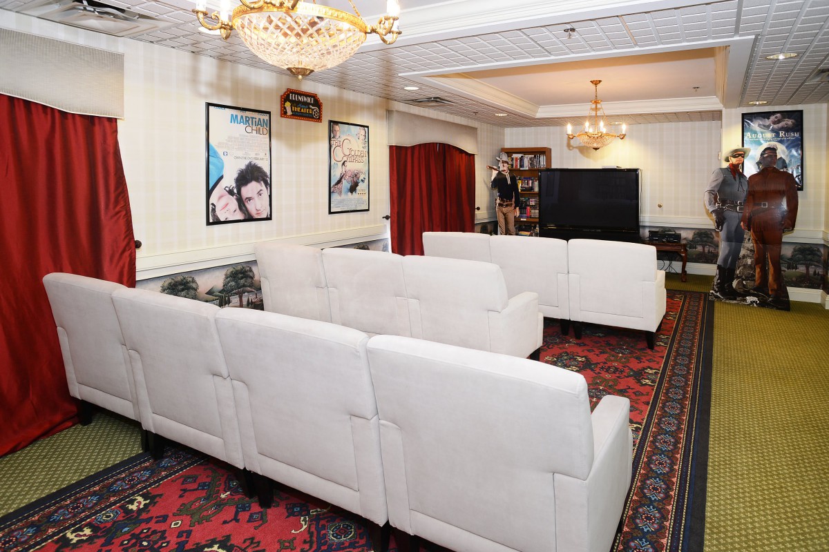 A spacious living room with white sofas, a chandelier, wall posters, and a large television.
