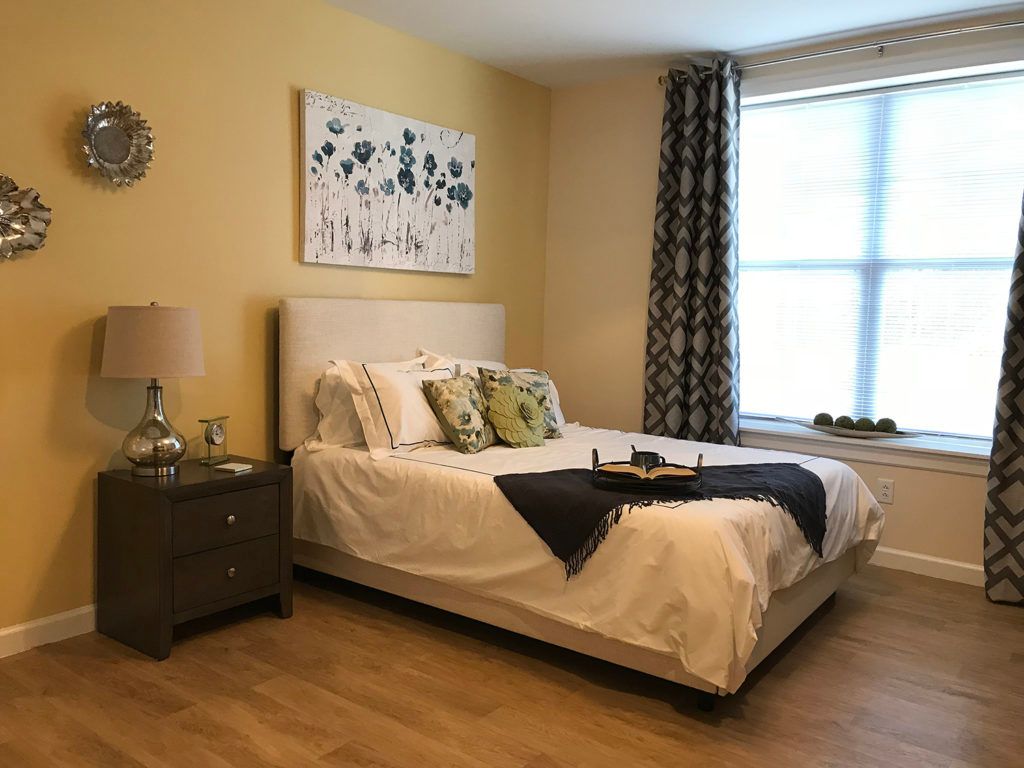 A cozy bedroom with a neatly made bed, decorative pillows, nightstand, and wall art.