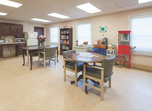 A well-lit room with tables, chairs, a bookshelf, and a popcorn machine.