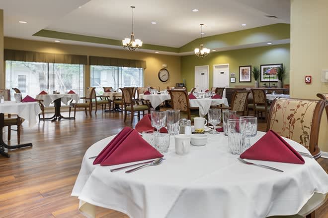 A spacious dining room with neatly set tables, featuring red napkins and glassware.