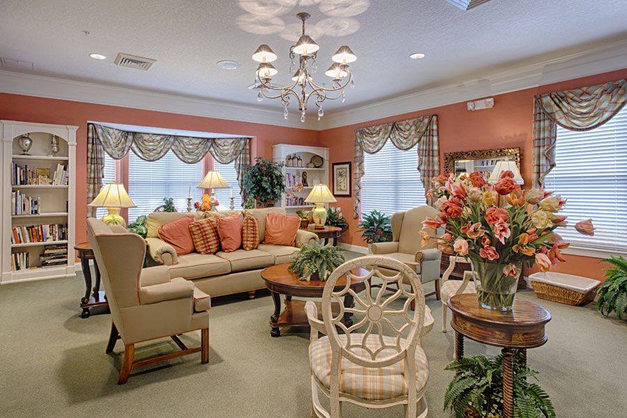 A cozy living room with elegant decor, featuring a large sofa, chandelier lighting, and floral arrangements.