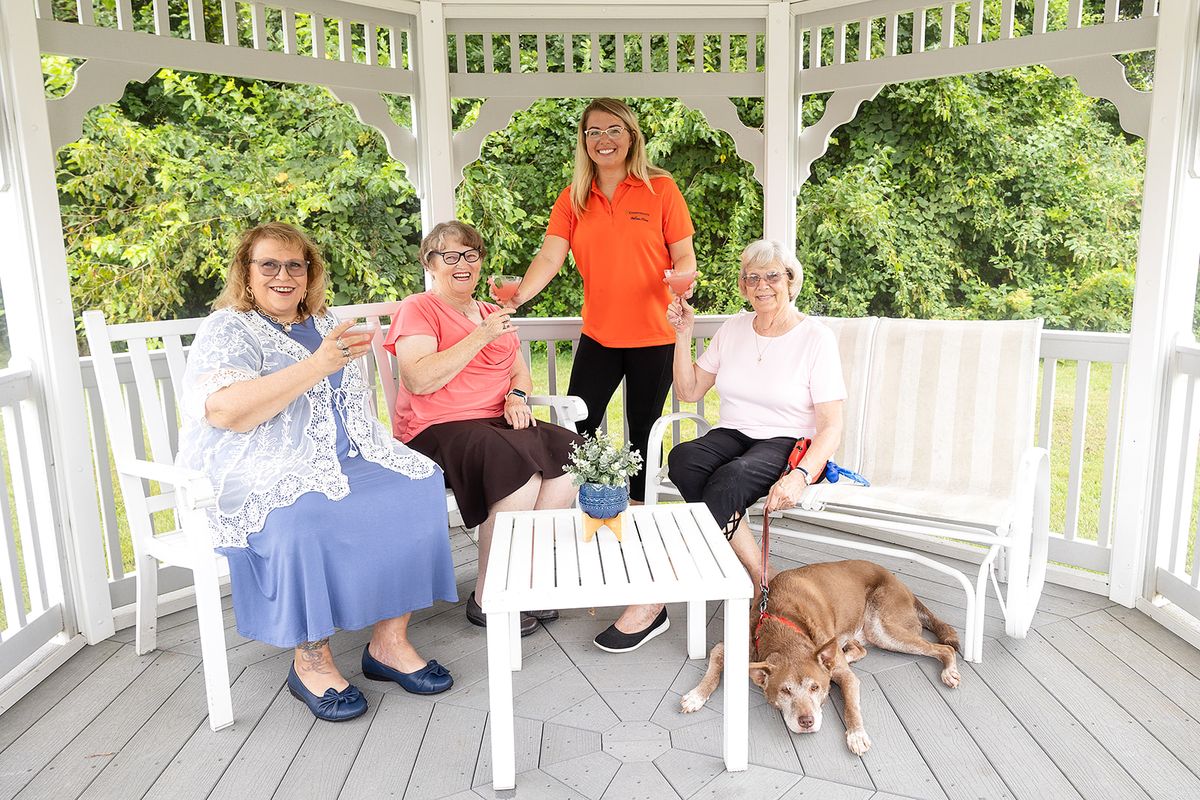 A group of women enjoying tea together in an outdoor gazebo, accompanied by a dog.