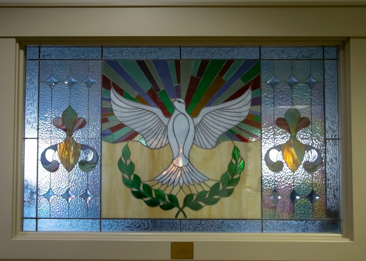 A beautiful stained glass window featuring a dove, symbolizing peace, adorned with colorful rays and floral patterns.