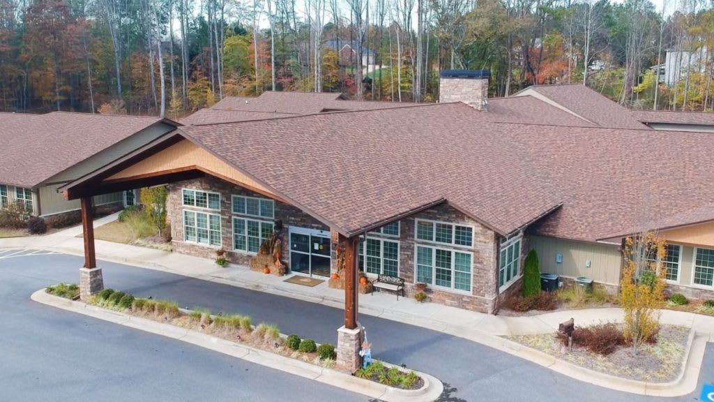 Aerial view of a building surrounded by trees, featuring a spacious parking lot and a prominent entrance.