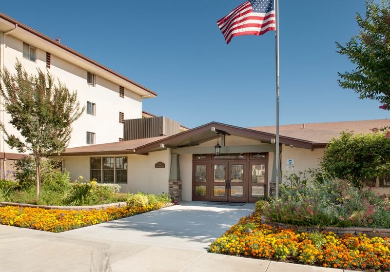 A building entrance with a garden and an American flag waving above.