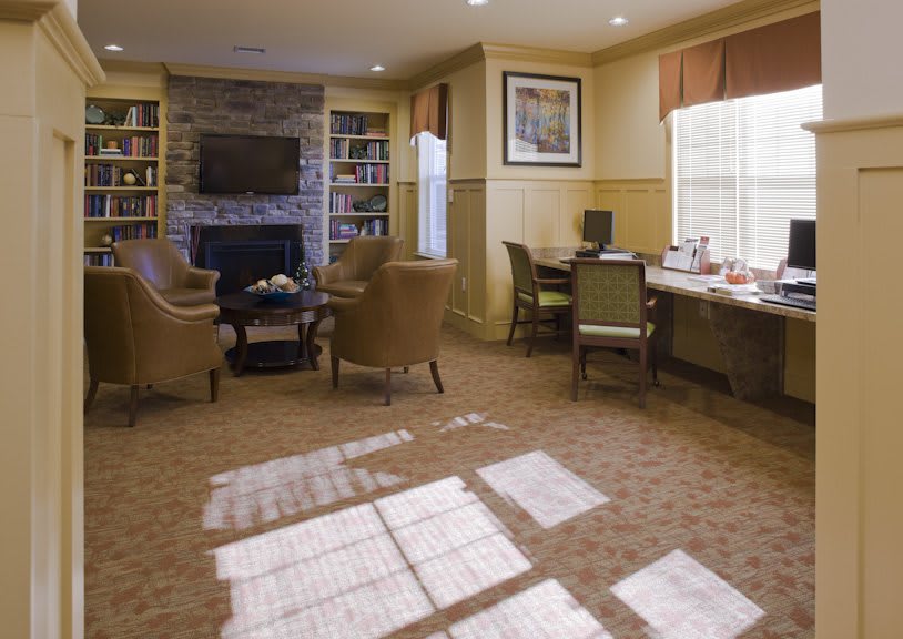 A cozy living room with comfortable seating, a fireplace, bookshelves, and natural light streaming in through the windows.