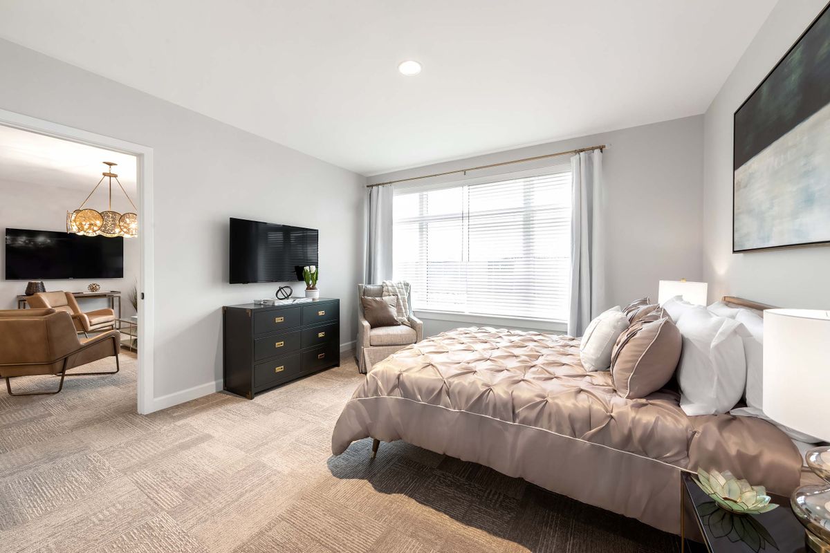 A modern bedroom with a large window, featuring a comfortable bed and a TV mounted on the wall.