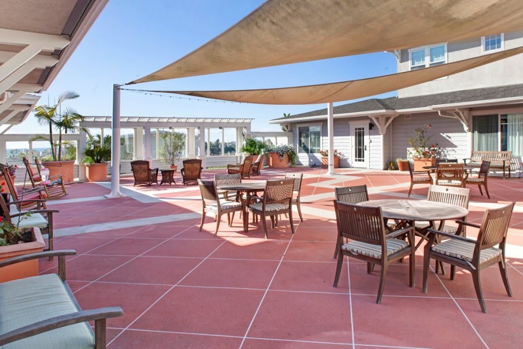 A sunny outdoor patio with tables and chairs, shaded by large sail-like canopies.