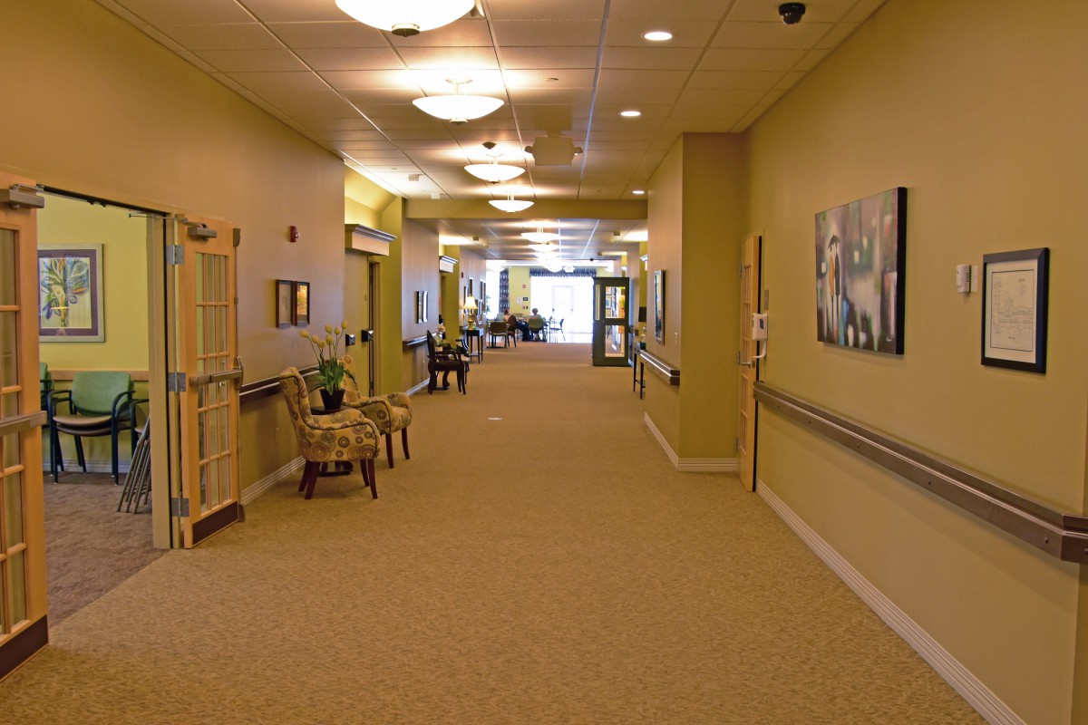 A well-lit corridor with chairs and artwork on the walls, likely in a hospital or nursing home.