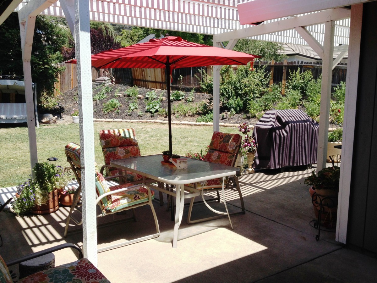 A cozy backyard patio setup with a table, chairs, and a red umbrella providing shade.