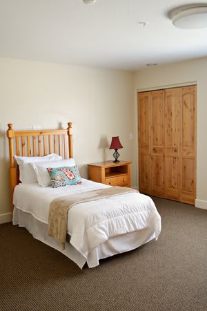 A minimalist bedroom featuring a single bed, wooden nightstand, and a cozy lamp.