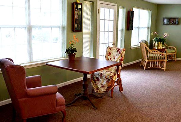 A cozy room with a wooden table, floral-patterned chairs, and large windows letting in natural light.