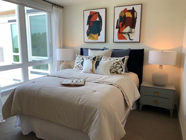 A modern bedroom with abstract artwork above the bed, featuring a cozy setup with pillows and bedside lamps.
