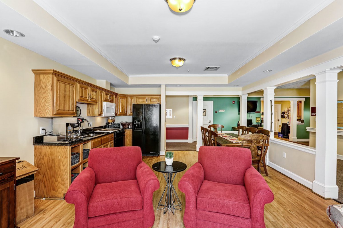 A modern open-concept living space featuring a kitchen, dining area, and two red armchairs in the foreground.