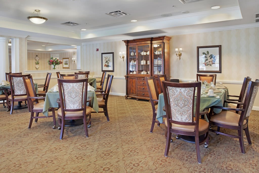 A well-furnished dining room featuring elegant chairs and tables, with a wooden cabinet and decor on the walls.