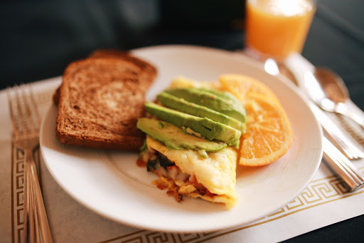 A delicious breakfast plate featuring a savory omelette topped with fresh avocado, served alongside toasted bread and orange slices.