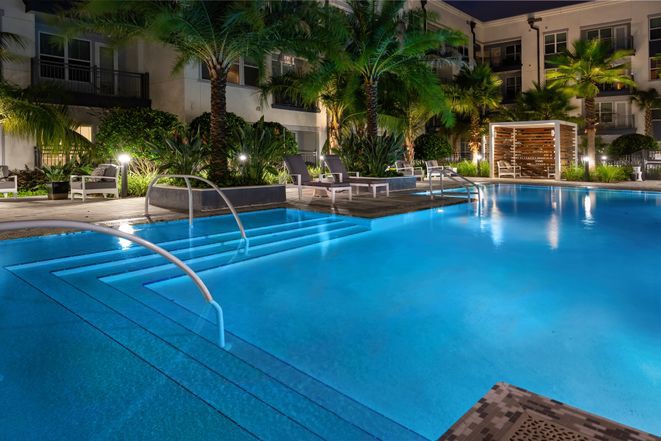 A serene outdoor swimming pool illuminated at night, surrounded by palm trees and resort lights.