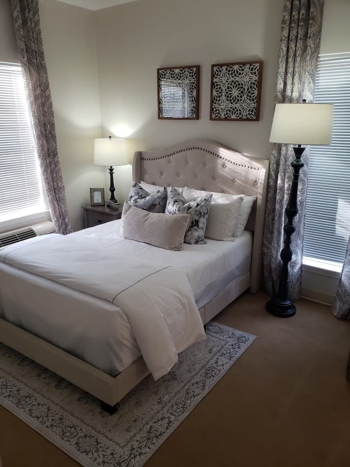 A cozy bedroom with a neatly made bed, two elegant lamps, and decorative wall art.