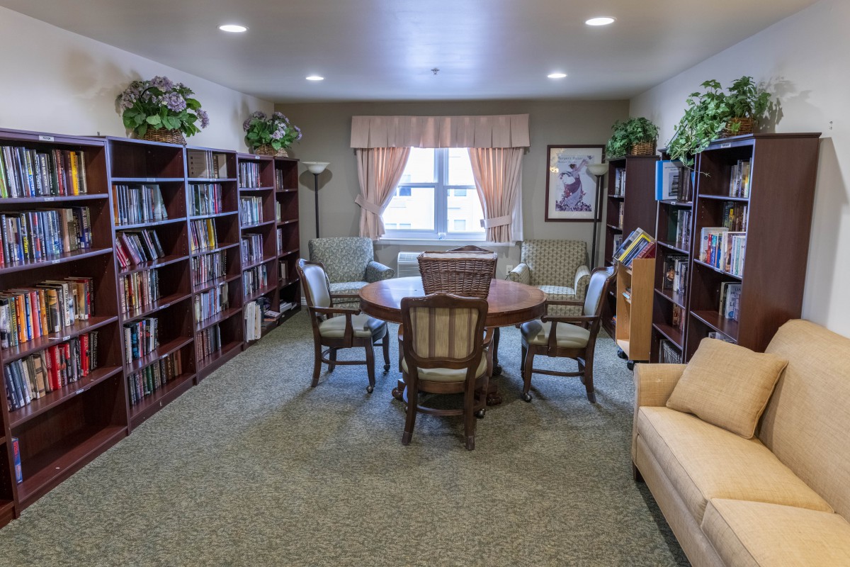 A cozy library reading room with bookshelves and seating around a central table.