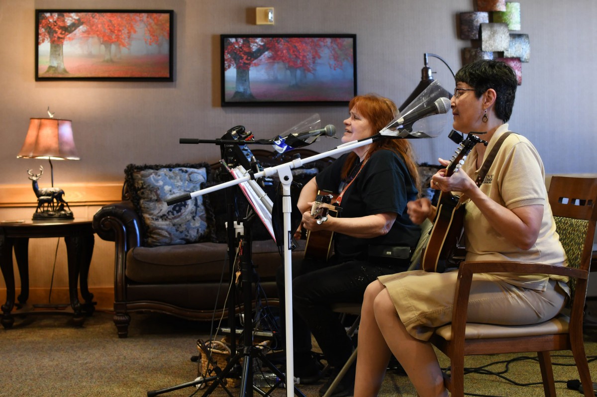 A cozy indoor performance featuring female musicians playing acoustic guitars and singing into microphones.