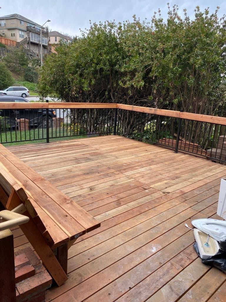 A newly constructed wooden deck with railing in a backyard setting.